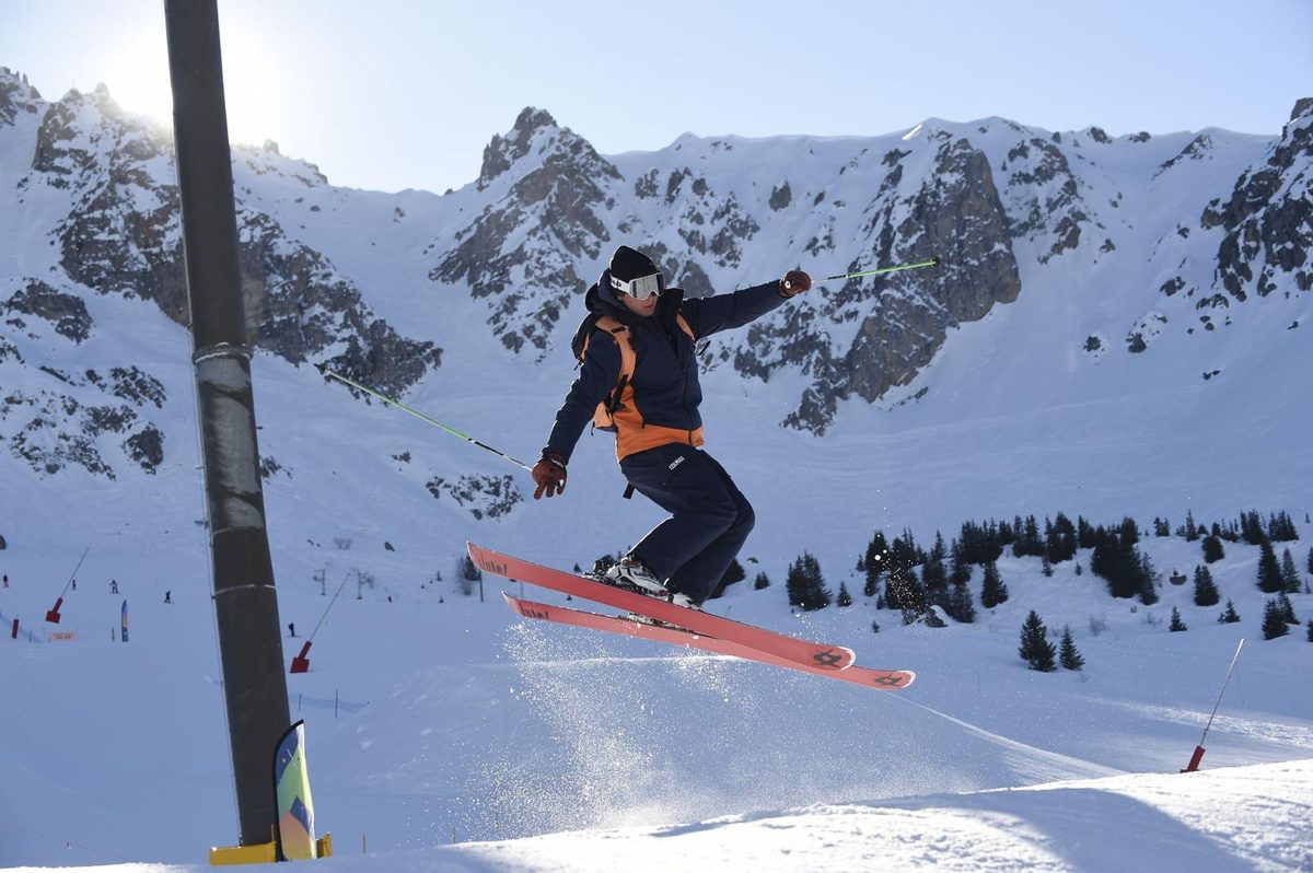 Instructor jumping on skis below steep rocky couloirs