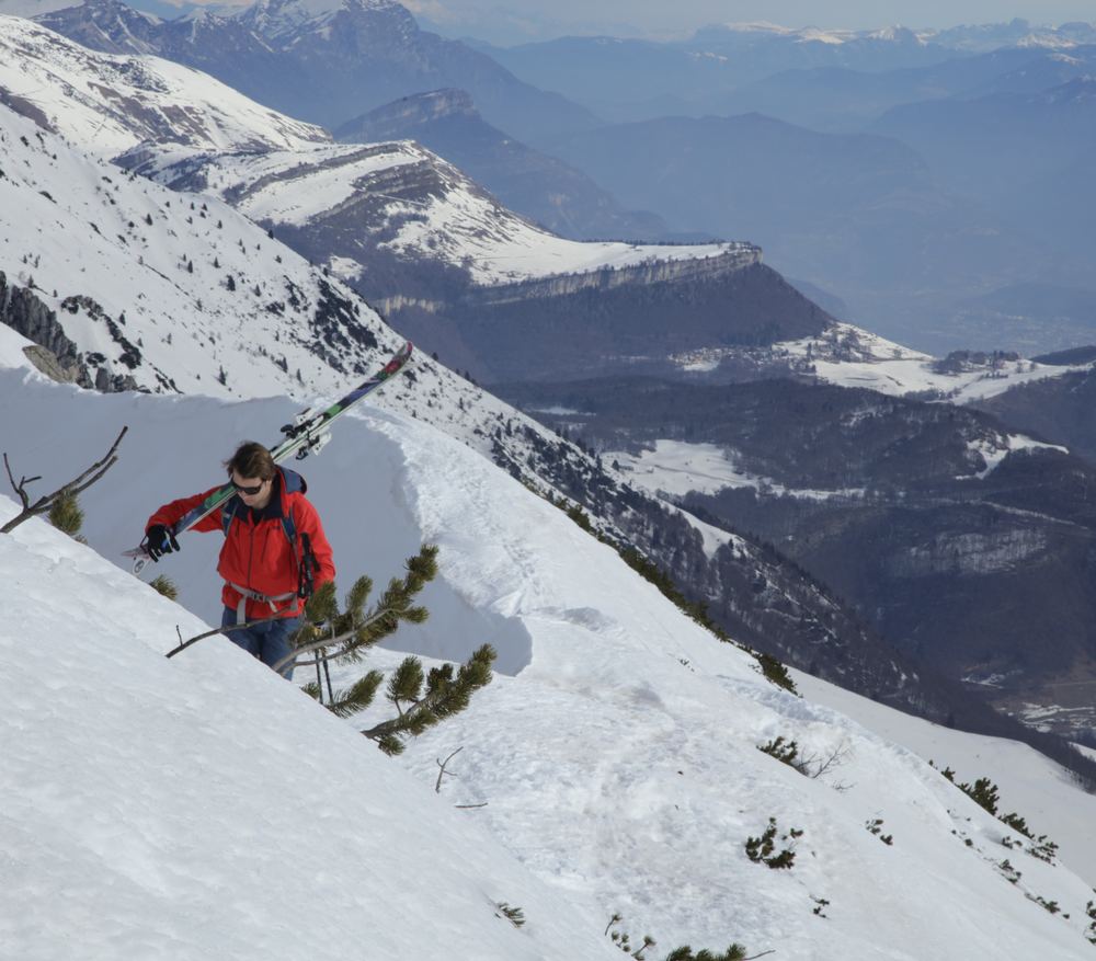 Skier climbing a snowy ridge with skis on his shoulder, valleys below