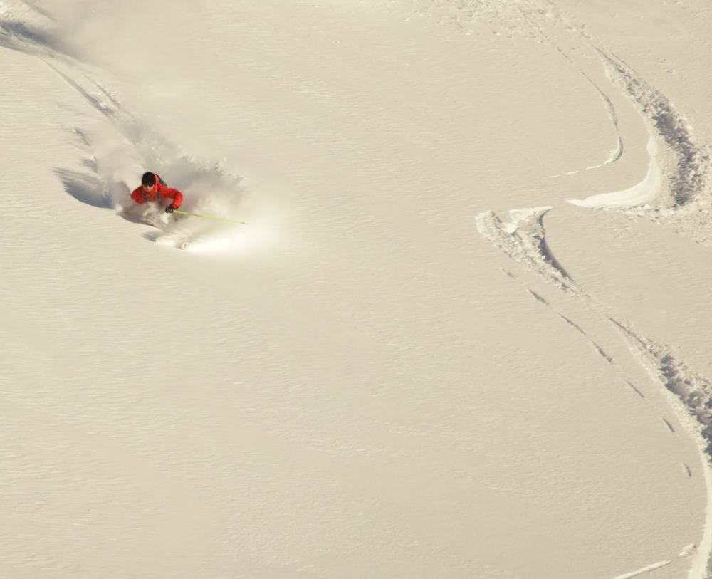 Skier carving through fresh powder, leaving S-shaped tracks