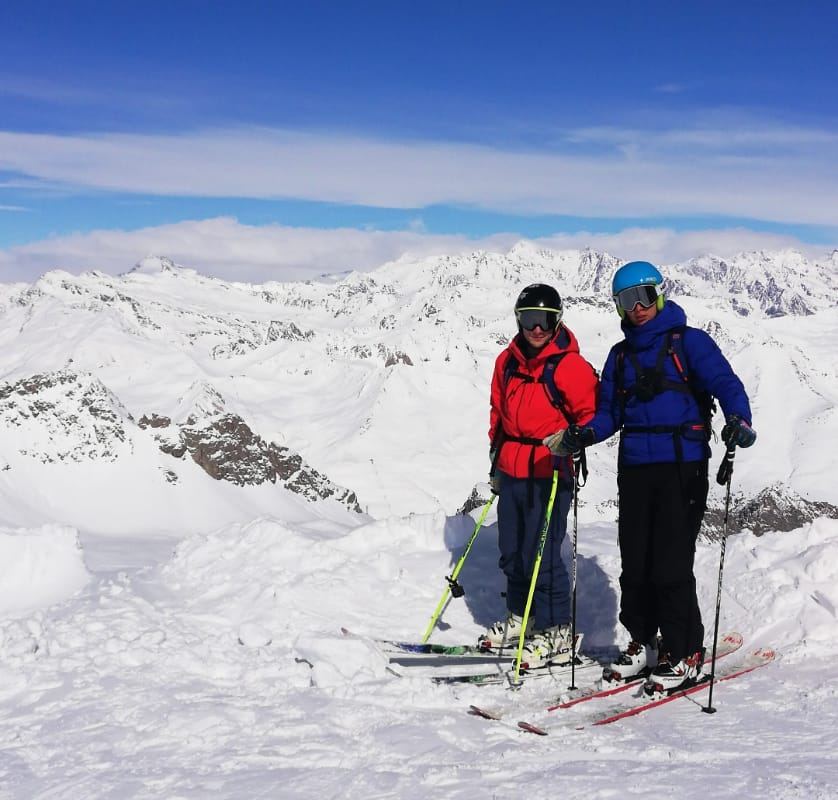 Two skiers on a summit with snowy peaks stretching to the horizon